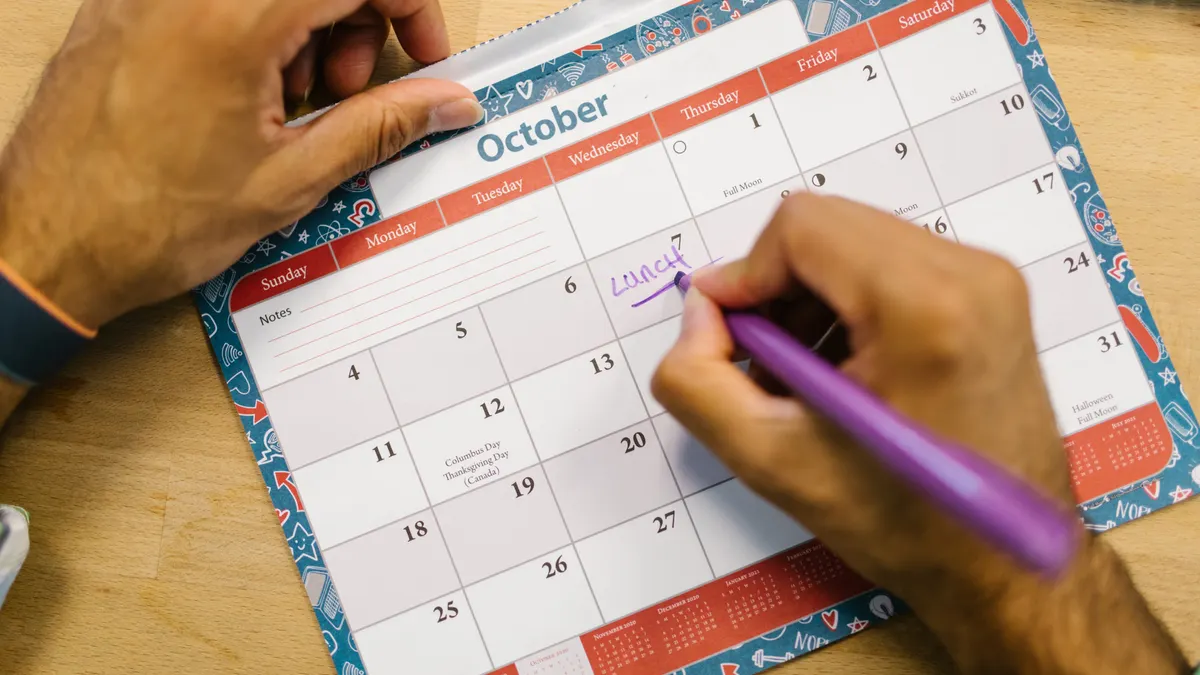 Hands writing on an October calendar page